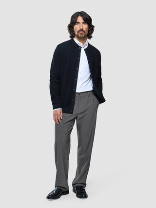 Ein Mann, der eine dunkelblaue Strickjacke mit Knöpfen über einem weißen Hemd trägt und dazu eine „Ease Pants Relaxed Fit“ in Dunkelgrau mit 360°-Stretch.