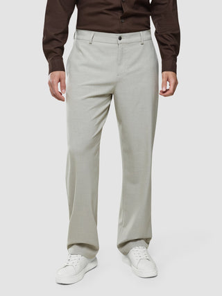 Ein Mann, der ein dunkelbraunes Hemd mit Knöpfen, eine „Ease Pants Relaxed Fit Sahara“ und weiße Sneaker trägt.