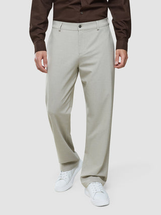 Eine Person, die ein braunes Hemd mit Knöpfen trägt, das in eine hellbeige „Ease Pants Relaxed Fit Sahara“ gesteckt ist, dazu weiße Sneaker.