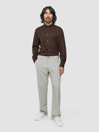 Ein Mann, der ein dunkelbraunes Hemd mit Knöpfen, eine „Ease Pants Relaxed Fit Sahara“ und weiße Sneaker trägt.