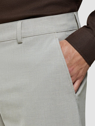 Eine Person, die ein braunes Hemd trägt, das in die Ease Pants Relaxed Fit Sahara gesteckt ist, und die Hand in der Seitentasche hat.