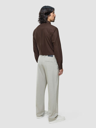 Ein Mann, von hinten gesehen, der ein braunes Hemd mit Knöpfen trägt, das in eine „Ease Pants Relaxed Fit Sahara“ gesteckt ist, sowie weiße Sneaker.