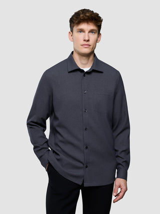 Ein Mann, der ein wasserabweisendes, anthrazitfarbenes „Effortless Shirt Dark Grey“ mit Brusttasche zu einer schwarzen Hose trägt.