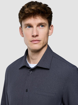 Ein Mann, der ein wasserabweisendes „Effortless Shirt“ in Dunkelgrau über einem weißen Unterhemd trägt.