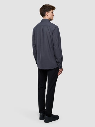 Ein Mann, von hinten gesehen, der ein wasserabweisendes, anthrazitfarbenes „Effortless Shirt Dark Grey“, eine schwarze Hose und dunkle Sneaker trägt.