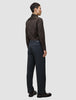 Eine Person, von hinten gesehen, die ein langärmeliges, dunkelbraunes Elevated Shirt Regular-Hemd trägt, das in eine dunkelgraue Hose gesteckt ist, sowie dunkle Leder-Loafer.