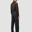 Eine Person, von hinten gesehen, die ein langärmeliges, dunkelbraunes Elevated Shirt Regular-Hemd trägt, das in eine dunkelgraue Hose gesteckt ist, sowie dunkle Leder-Loafer.