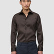 Ein Mann trägt ein dunkelbraunes Elevated Shirt Slim, das er in eine dunkelgraue Hose gesteckt hat.