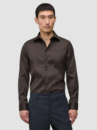 Ein Mann trägt ein dunkelbraunes Elevated Shirt Slim, das er in eine dunkelgraue Hose gesteckt hat.