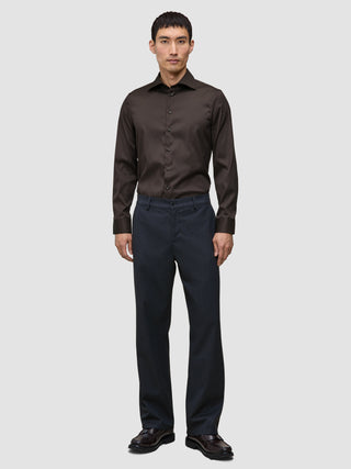 Ein Mann, der ein dunkelbraunes Elevated Shirt Slim, eine dunkle Hose und dunkle Lederschuhe trägt.