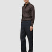 Ein Mann trägt das Elevated Shirt Slim in Dunkelbraun aus Pima-Baumwolle, dazu eine dunkle Hose und dunkle Schuhe.