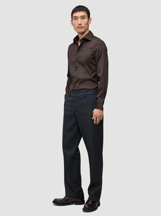 Ein Mann trägt das Elevated Shirt Slim in Dunkelbraun aus Pima-Baumwolle, dazu eine dunkle Hose und dunkle Schuhe.