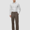 Ein Mann, der ein weißes, schmal geschnittenes Elevated-Hemd trägt, dazu eine braune Hose und dunkle Slipper.