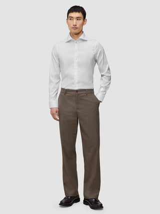 Ein Mann, der ein weißes, schmal geschnittenes Elevated-Hemd trägt, dazu eine braune Hose und dunkle Slipper.