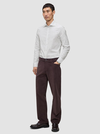 Ein Mann, der ein hellgrau gestreiftes Elevated Shirt Slim, eine dunkelbraune Hose und dunkle Slipper trägt.