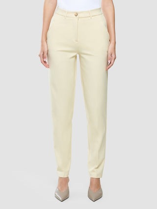 Eine Person, die eine „Women Essential Pants Tapered“ in der Farbe „Misty Yellow“ und Pumps mit spitzer Zehenpartie trägt.