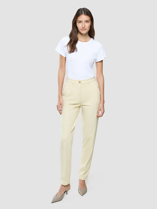 Eine Frau, die ein weißes T-Shirt und eine „Women Essential Pants Tapered“ in der Farbe „Misty Yellow“ trägt, die ein minimalistisches, skandinavisches Design widerspiegeln.