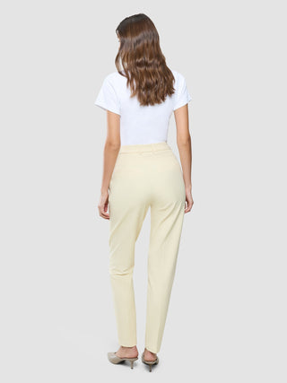 Eine Person, von hinten gesehen, die ein weißes T-Shirt, eine „Women Essential Pants Tapered“ in Misty Yellow und Pantoletten mit niedrigem Absatz trägt.