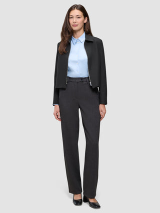Eine Frau trägt eine schwarze Essential Short Zip Jacket über einem hellblauen Hemd und einer grauen Hose.