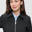 Eine Person, die eine schwarze Essential Short Zip Jacket über einem hellblauen Hemd mit Knöpfen trägt.