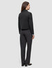 Eine Person, die von hinten zu sehen ist, trägt eine schwarze Essential Short Zip Jacket über einem hellblauen Hemd mit Kragen und einer dunkelgrauen Hose; das Design ist schlicht und minimalistisch.