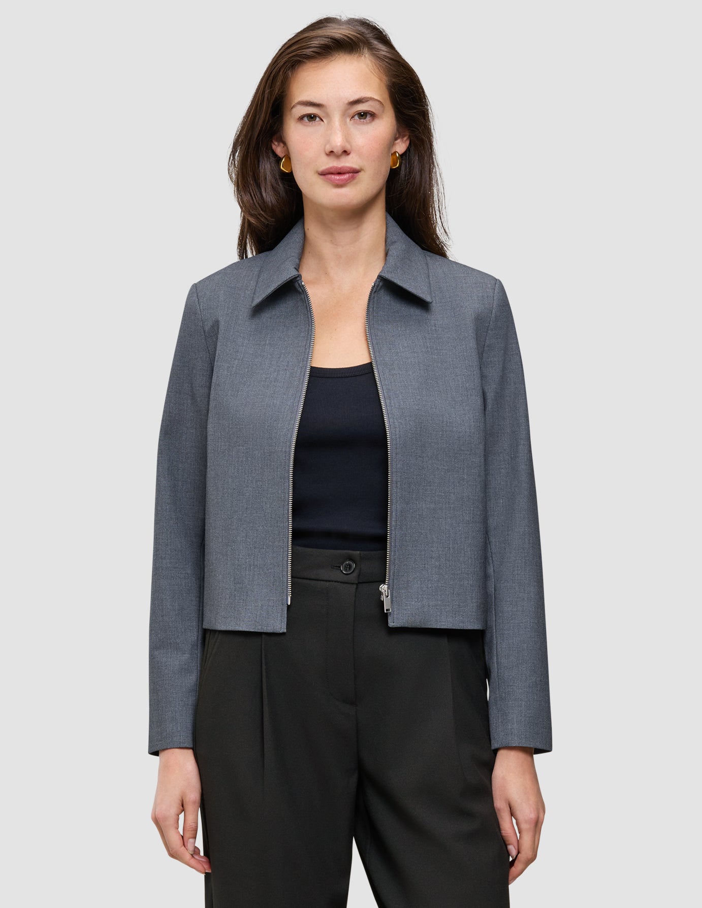 Eine Frau, die eine Essential Short Zip Jacket in Dunkelgrau-Melange über einem schwarzen Oberteil und einer schwarzen Hose trägt.