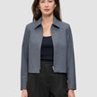 Eine Frau, die eine Essential Short Zip Jacket in Dunkelgrau-Melange über einem schwarzen Oberteil und einer schwarzen Hose trägt.