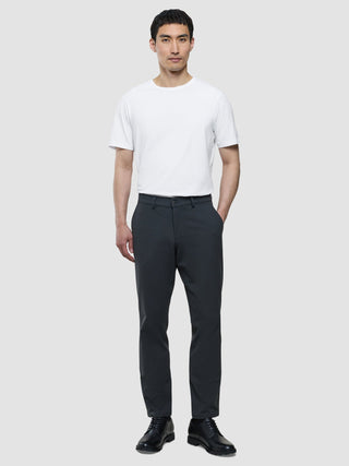 Ein Mann, der ein weißes T-Shirt und eine „Gen. 2.0 Pants Regular Signature Dark Grey“ trägt, steht vor einem hellgrauen Hintergrund.