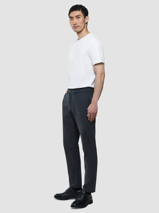 Ein Mann im Profil, der ein weißes T-Shirt, eine Hose „Gen. 2.0 Pants Regular Signature Dark Grey“ und schwarze Anzugschuhe trägt.