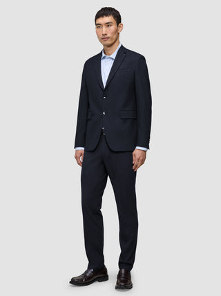 Ein Mann trägt einen Motion Blazer Regular in Mitternachtsblau mit 360°-Stretch und eine dazu passende Hose über einem hellblauen Hemd, dazu dunkle Loafer.