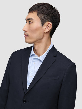 Eine Person im Profil, von der Brust aufwärts, die einen Motion Blazer Regular in Mitternachtsblau über einem hellblau gestreiften Hemd trägt.