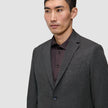 Ein Mann, der einen Motion Blazer Regular Pepper Grey über einem dunklen Hemd mit Knopfleiste trägt und damit ein klares, minimalistisches skandinavisches Design zur Geltung bringt.