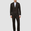 Ein Mann, der einen Motion Blazer Slim Cognac über einem weißen Hemd mit Kragen und schwarzen Anzugschuhen trägt und damit eine klare, skandinavische Designästhetik verkörpert.