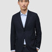 Ein Mann, der den Motion Blazer Slim Midnight Blue in Dunkelblau über einem hellblauen Nadelstreifenhemd trägt und damit das klare skandinavische Design zur Geltung bringt.