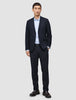 Ein Mann, der einen Motion Blazer Slim in Mitternachtsblau trägt, dazu ein hellblaues Button-Down-Hemd, eine dunkelblaue Hose, einen schwarzen Gürtel und dunkle Slipper.
