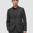 Ein Mann, der einen Motion Blazer Slim in der Farbe Pepper Grey über einem dunklen Hemd mit Knöpfen trägt und damit skandinavisches Design zur Geltung bringt.