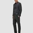 Ein Mann, der einen Motion Blazer Slim in der Farbe Pepper Grey mit einer dazu passenden Hose, einem dunklen Hemd und dunklen Loafern im klaren, skandinavischen Design trägt.