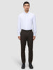 Ein Mann in einem weißen Hemd und einer Motion Suit-Hose in der Farbe Regular Cognac, kombiniert mit schwarzen Schuhen für einen eleganten Look.