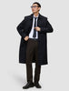 Ein Mann trägt einen schwarzen Mantel, ein weißes Hemd und eine dunkle Krawatte sowie die Motion Suit Pants Regular Cognac – eine elegante, braune Anzughose mit 360°-Stretch.