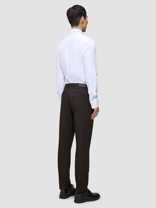 Eine Person, von hinten gesehen, die ein weißes Hemd, eine Motion Suit-Hose in der Passform Regular in der Farbe Cognac und schwarze Anzugschuhe trägt und damit einen eleganten Look präsentiert.
