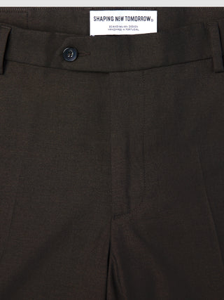 Nahaufnahme einer braunen Motion Suit-Hose in der Passform Regular in der Farbe Cognac mit Knopfverschluss und einem Etikett am Bund mit der Aufschrift SHAPING NEW TOMORROW, SCANDINAVIAN DESIGN, HANDMADE IN PORTUGAL.