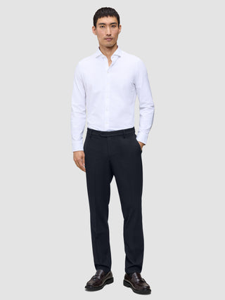 Ein Mann, der ein weißes Hemd, eine Motion Suit-Hose in der Passform Regular in Mitternachtsblau mit 360°-Stretch sowie dunkle Slipper trägt.