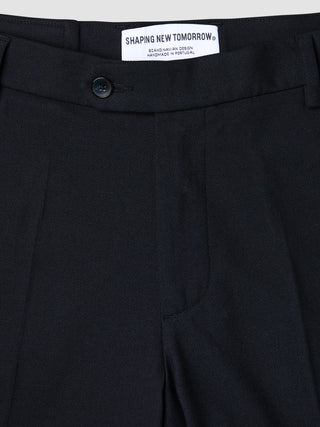 Nahaufnahme einer atmungsaktiven, dunkelblauen Motion Suit-Hose in Regular-Passform in Mitternachtsblau mit 360°-Stretch, Knopfverschluss und einem Innenetikett mit der Aufschrift Shaping New Tomorrow, Scandinavian Design und Handmade in Portugal.