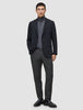 Ein Mann, der einen schwarzen Blazer, einen grauen Rollkragenpullover, eine Motion Suit-Hose in der Passform Regular in der Farbe Pepper Grey sowie schwarze Slipper trägt.