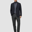 Ein Mann, der einen schwarzen Blazer, einen grauen Rollkragenpullover, eine Motion Suit-Hose in der Passform Regular in der Farbe Pepper Grey sowie schwarze Slipper trägt.