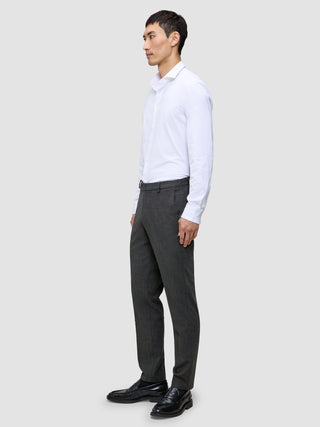 Ein Mann in einem weißen Hemd und einer grauen Motion Suit-Hose in der Farbe Regular Pepper Grey steht im Profil und trägt schwarze Slipper.