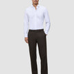 Ein Mann, der ein weißes, langärmeliges Hemd mit Knöpfen und eine Motion Suit Pants Relaxed Cognac sowie dunkle Loafer trägt.