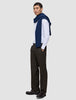 Ein Mann trägt ein weißes, fein gestreiftes Hemd mit Knöpfen, einen marineblauen Pullover, der über seinen Schultern liegt, sowie die Motion Suit Pants Relaxed Cognac – eine dunkelbraune Anzughose mit 360°-Stretch und lockerer Passform.
