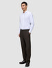 Ein Mann in einem weißen Hemd und einer braunen, locker sitzenden Motion Suit-Hose Relaxed Cognac steht da, eine Hand in der Hosentasche.