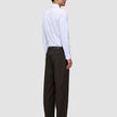 Eine Person in einem weißen Hemd und einer Motion Suit-Hose Relaxed Cognac, im Profil stehend.